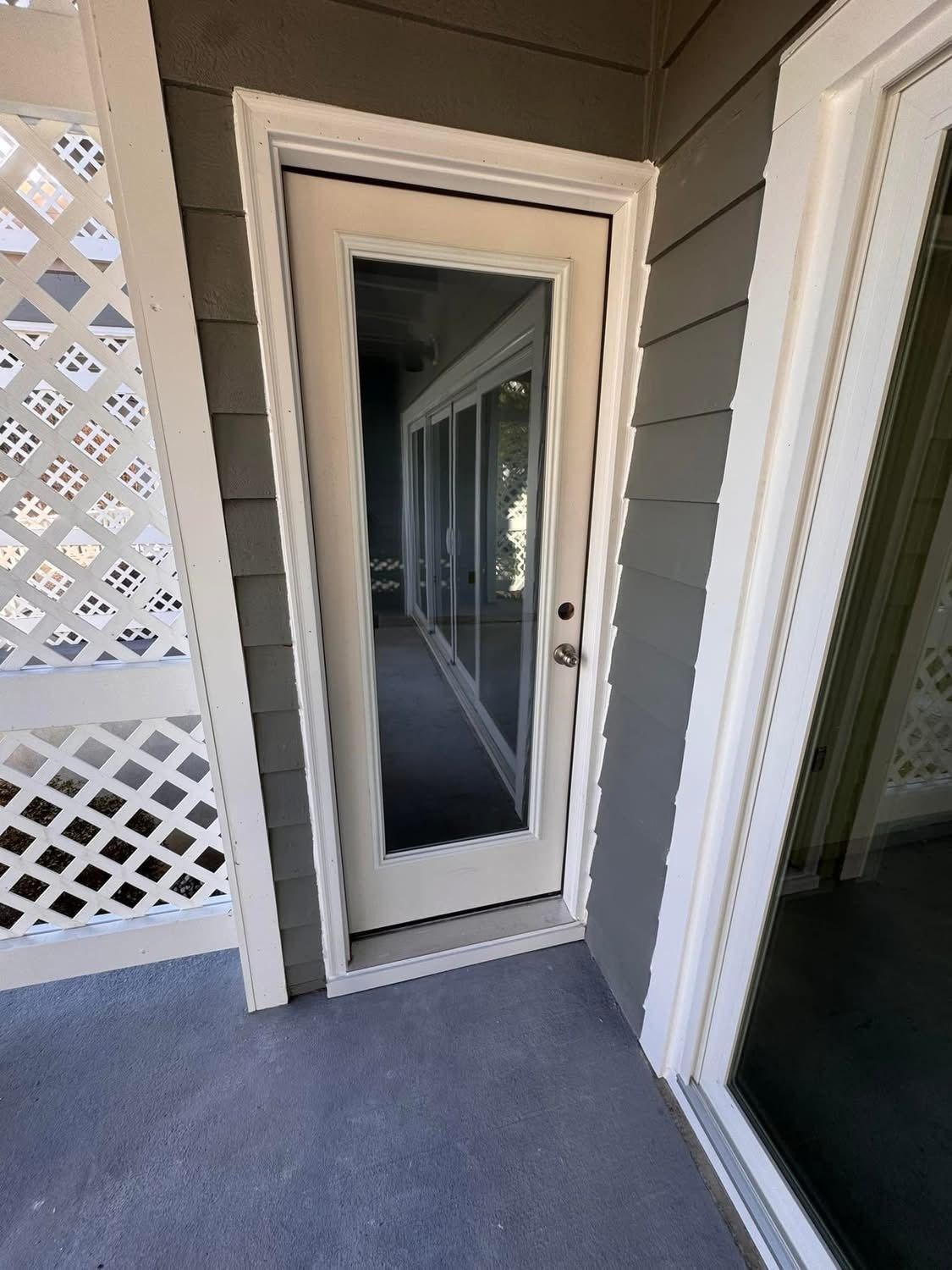 Exterior view of a door with glass panels, surrounded by gray siding and white trim.  A lattice wall is on the left.