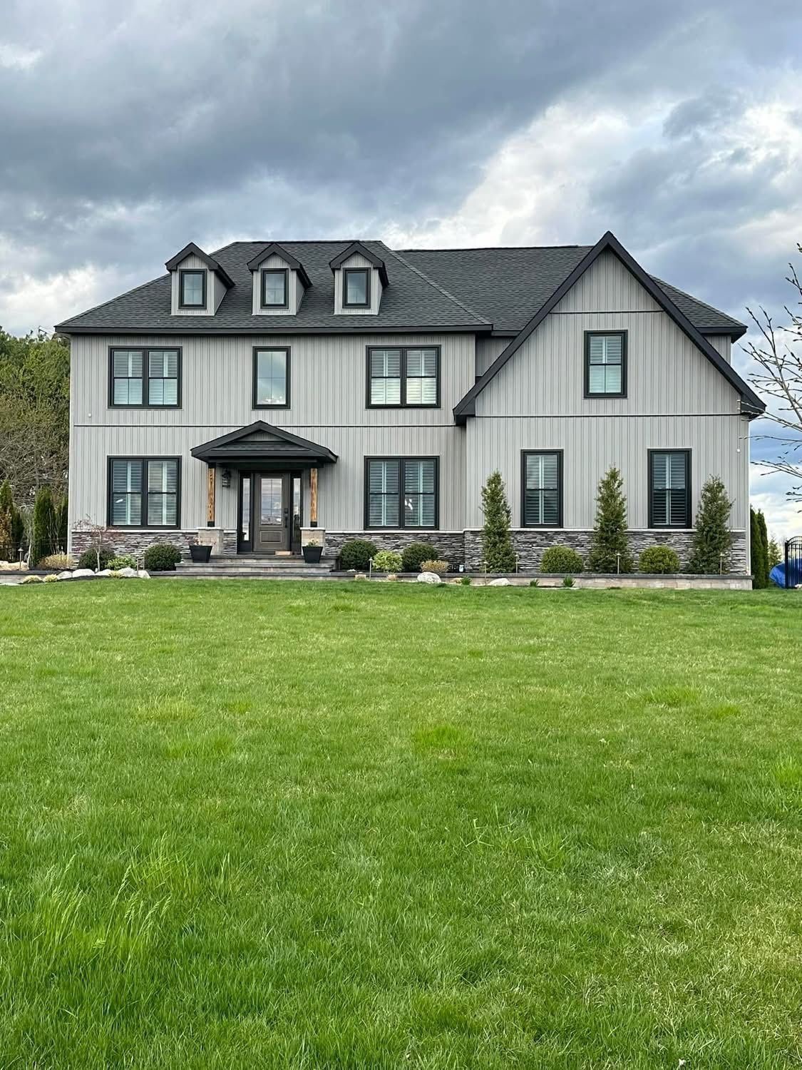 Two-story house with gray siding, black windows, and a green lawn. Cloudy sky.
