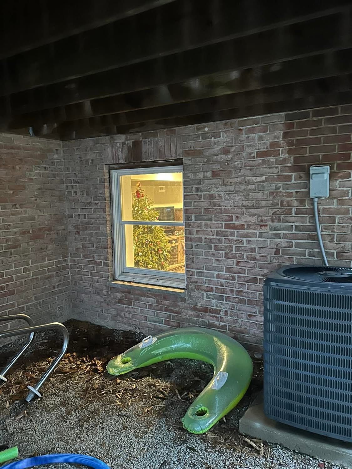 Brick exterior wall with a window, air conditioner, and green plastic toy.