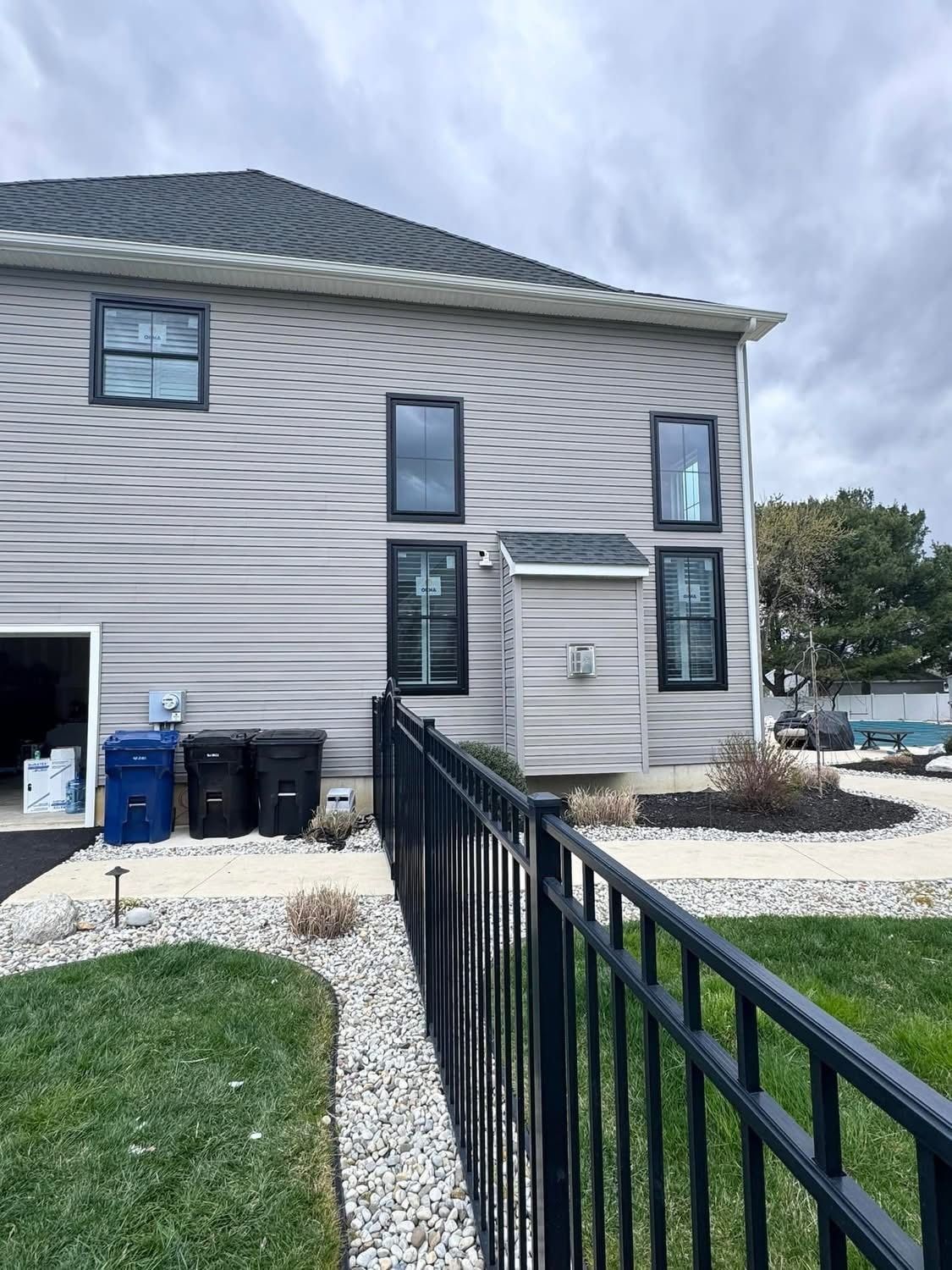 Gray two-story house with black windows. Black fence and green lawn in front. Overcast sky.