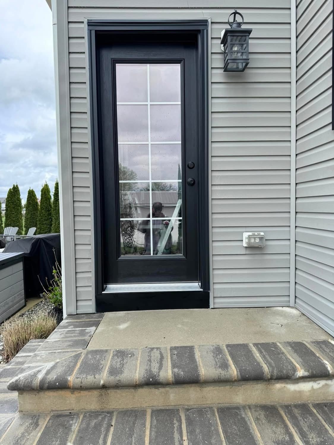 Black door with glass panel, gray siding, and porch steps. Exterior with a light fixture.