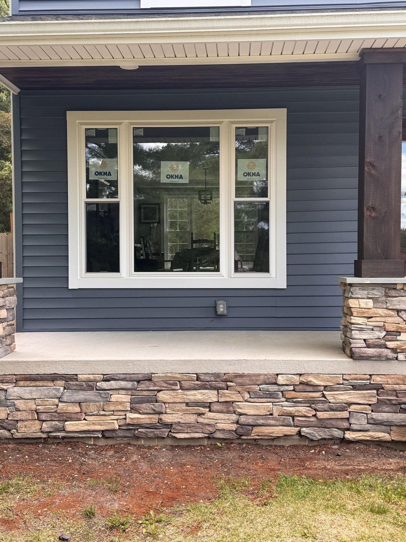 Exterior of a house with dark blue siding, a white-framed window, and stone accents.