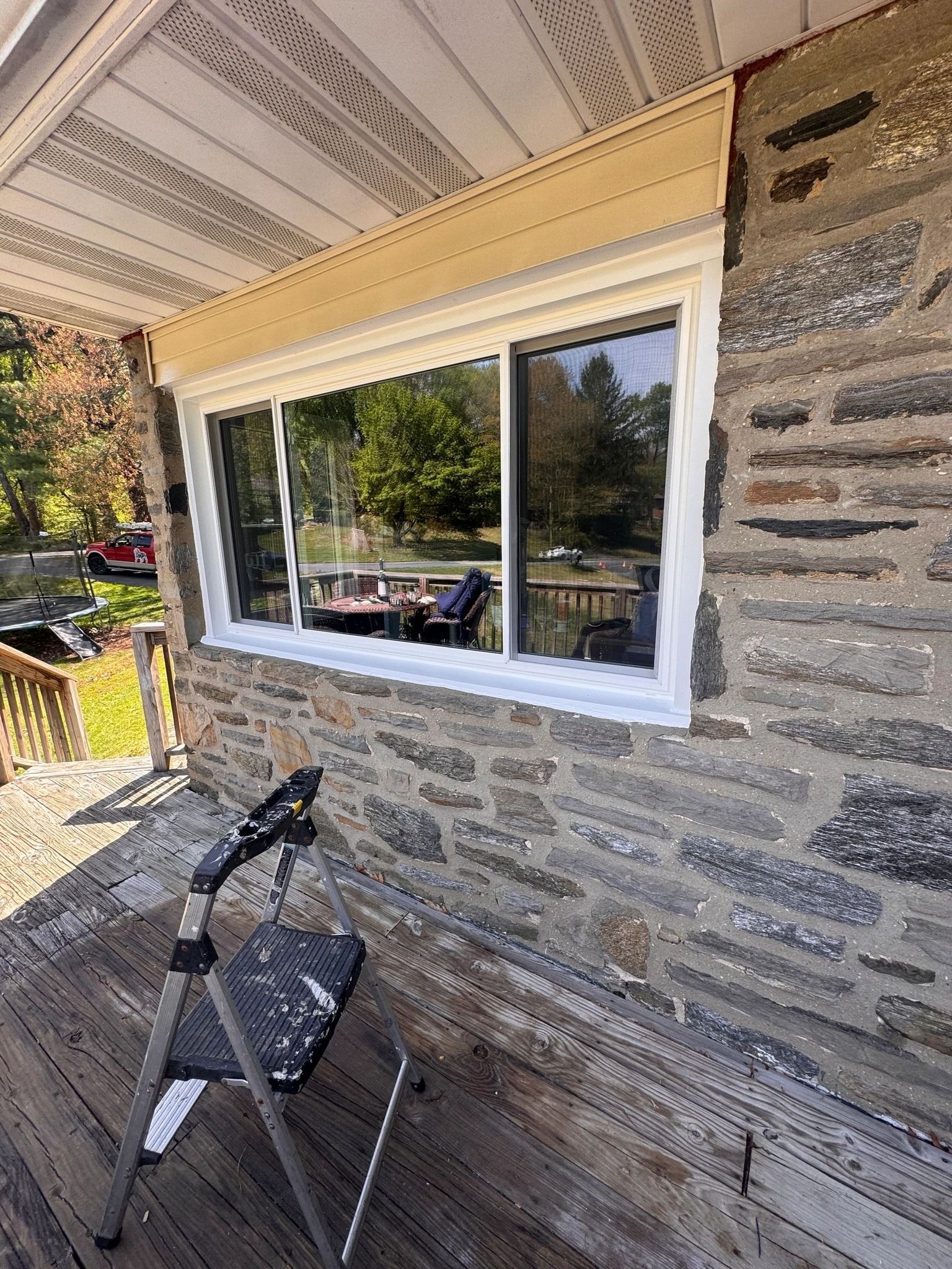 Window replacement on a stone wall exterior. White-framed sliding window with beige trim. A ladder sits below.