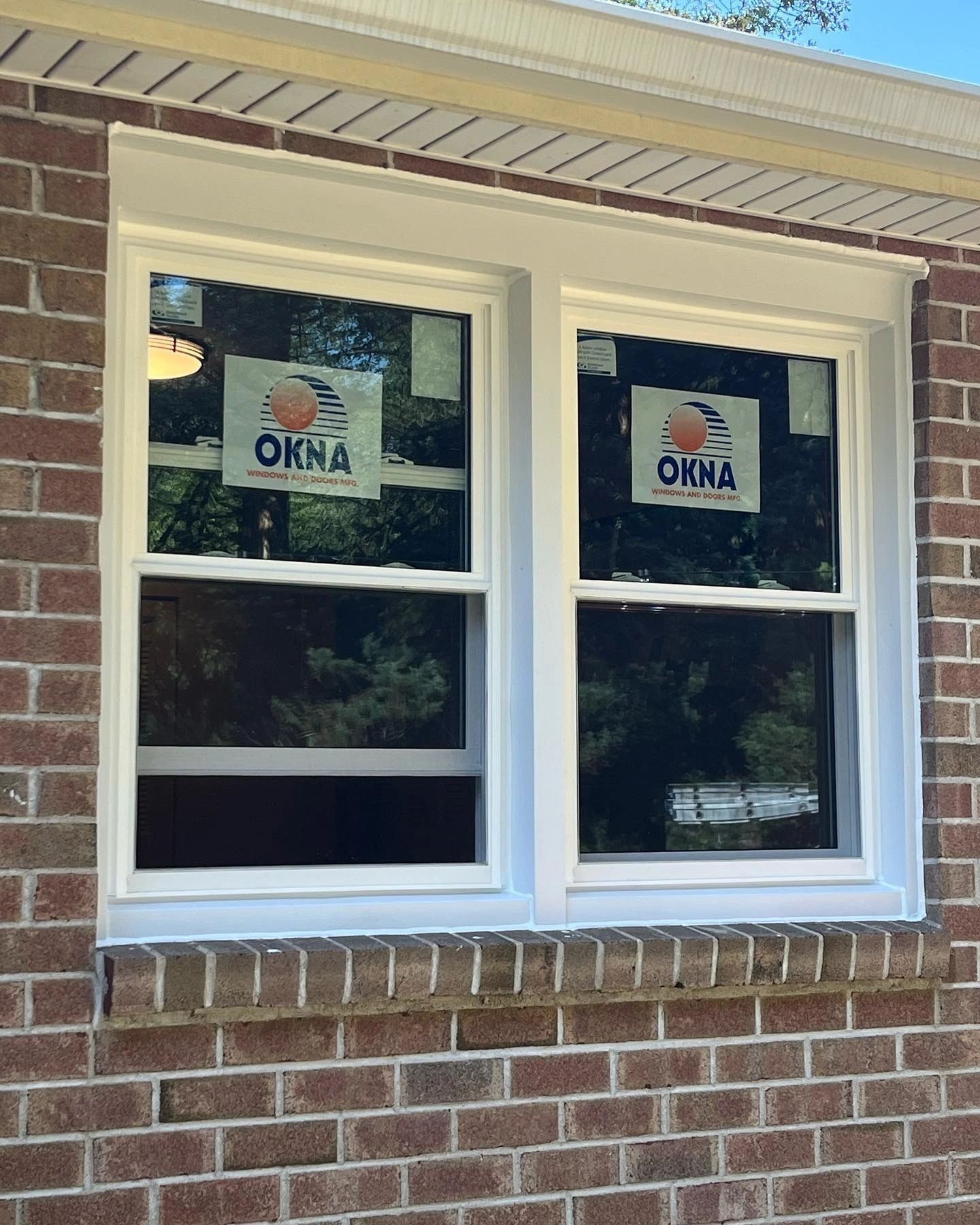 Two white framed windows with new window stickers installed in a brick wall.