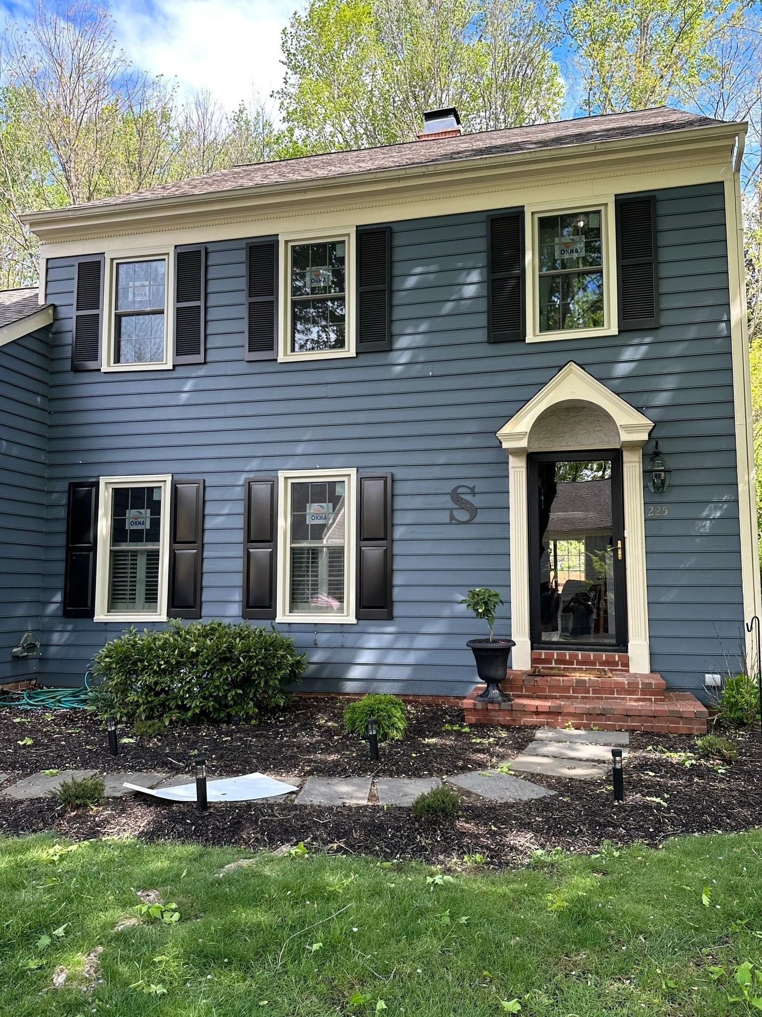 Blue house with black shutters, beige trim, and a black front door under an arched portico.