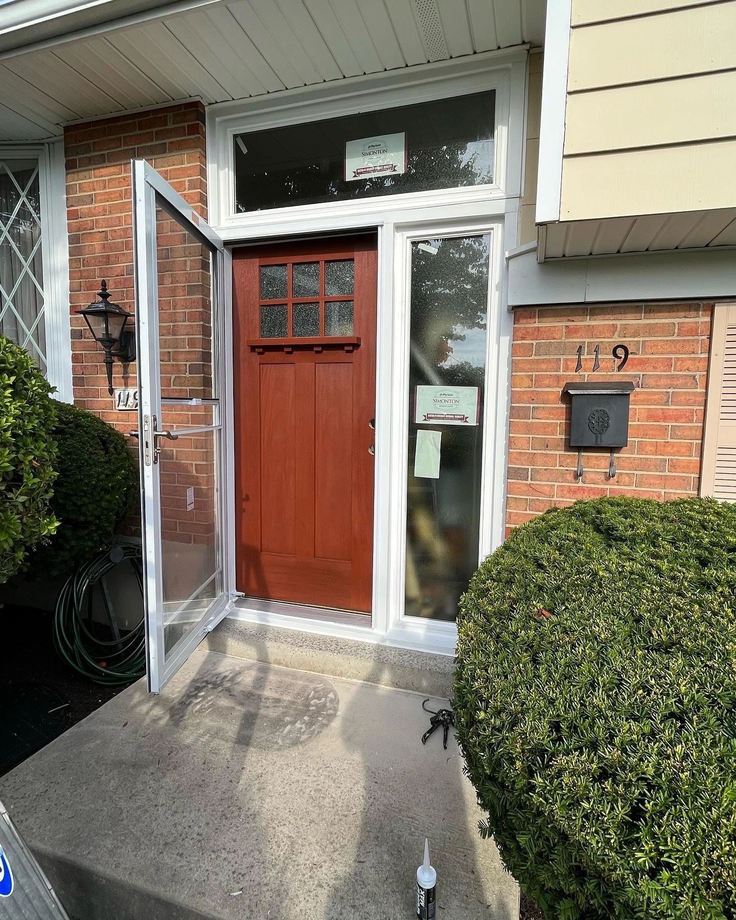 Red door with sidelight and transom, open screen door, brick exterior, house number 119.