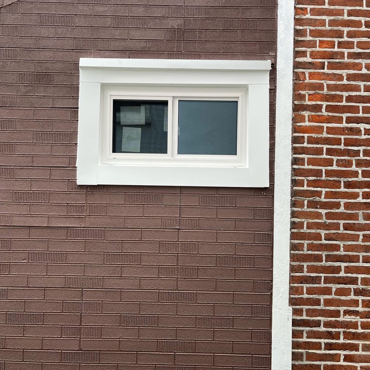 White-framed window on a red-brown brick wall, next to a red brick wall with white border.