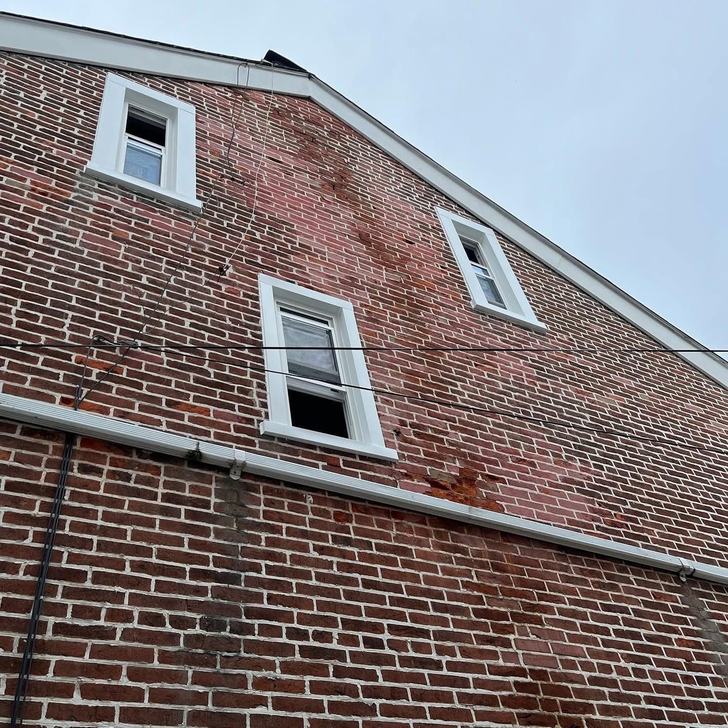 Brick building with three windows, white trim, and a cloudy sky.