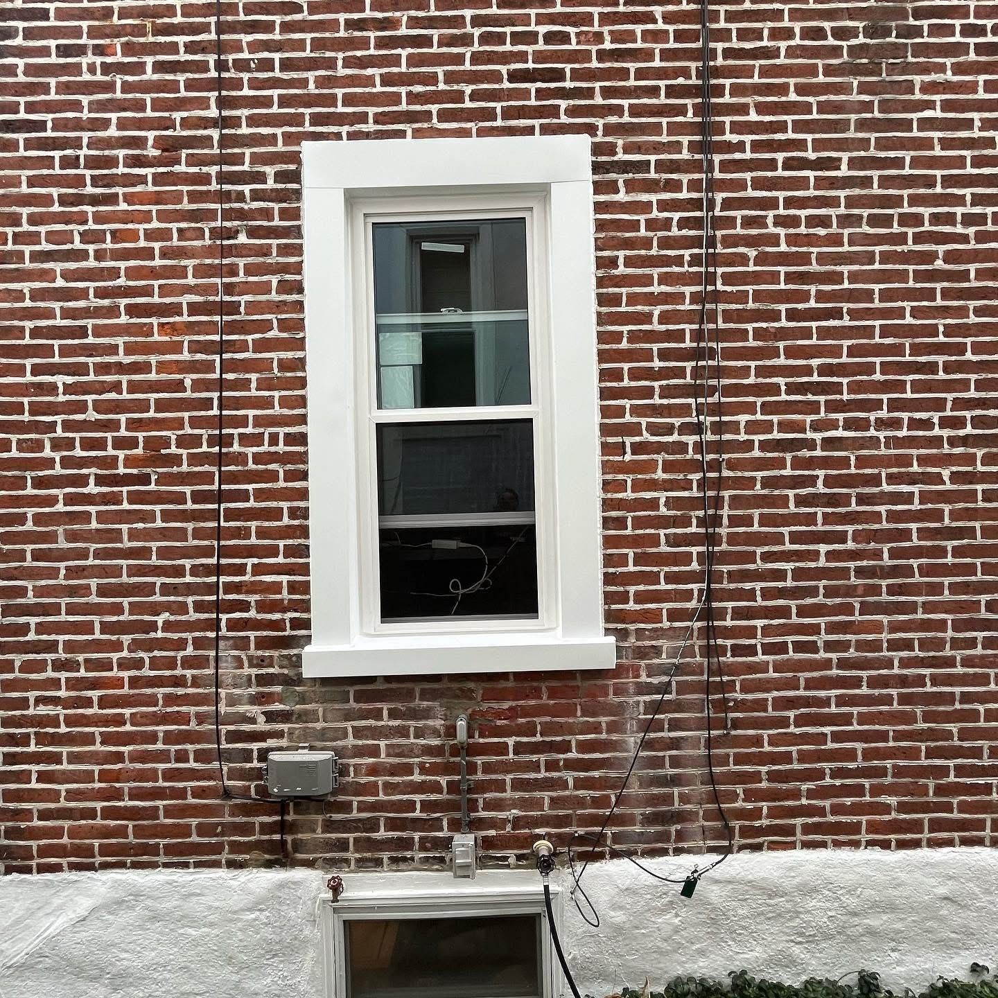 Brick wall with white framed window and wires.