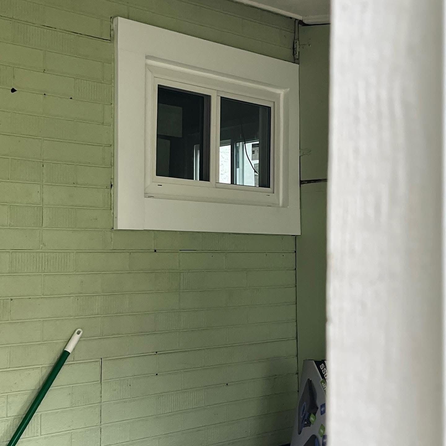 White-framed window on a green-painted wall, partially obscured by a white vertical support.