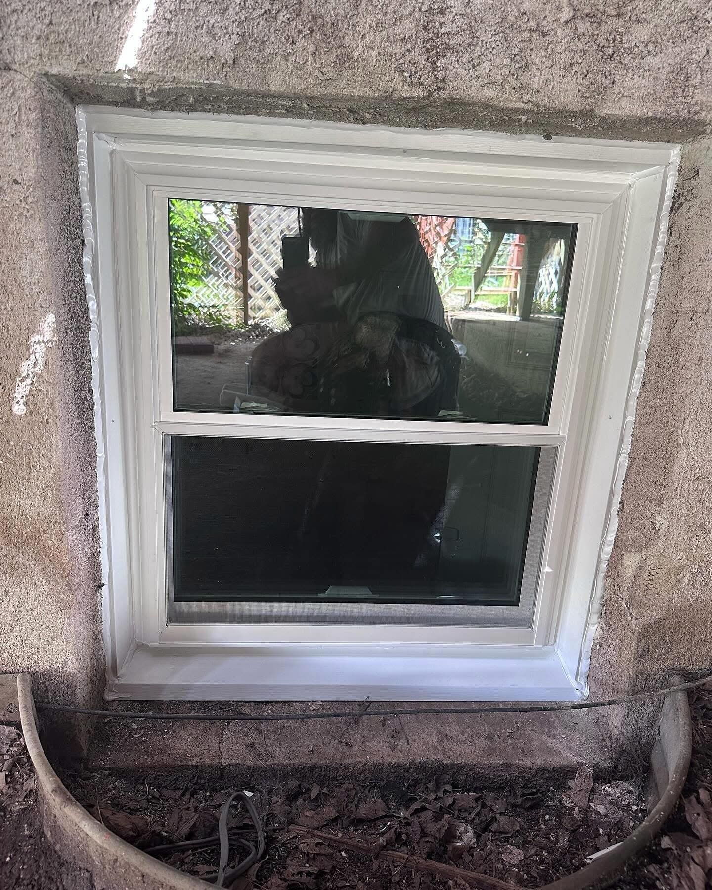 White-framed window in a textured stucco wall. The glass reflects a blurry outdoor scene.