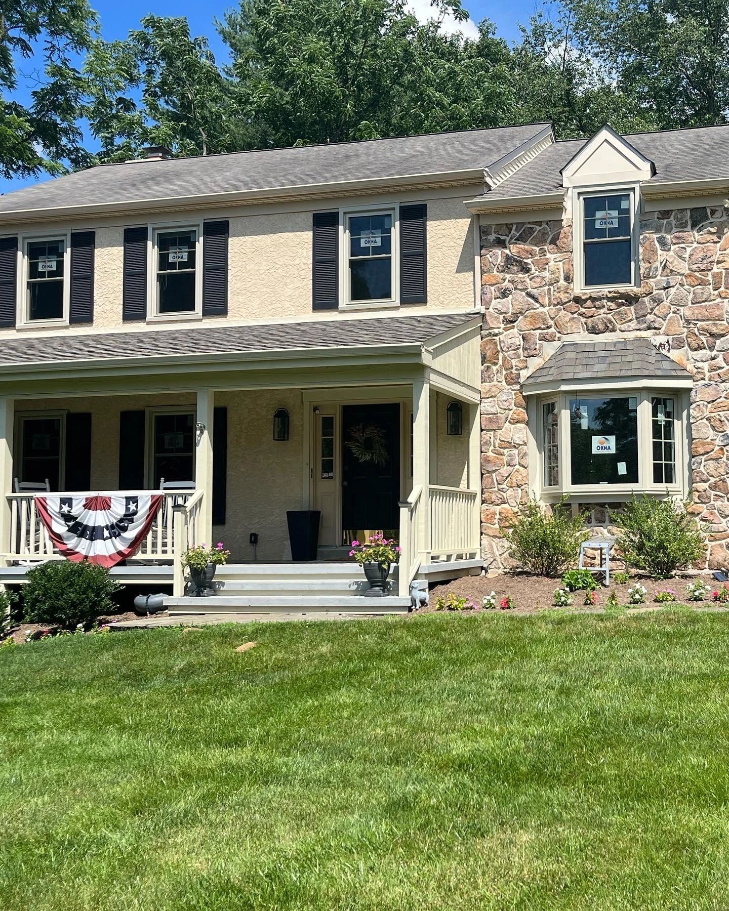 Two-story house with stone facade, beige trim, shutters, a porch, bay window, and a green lawn.