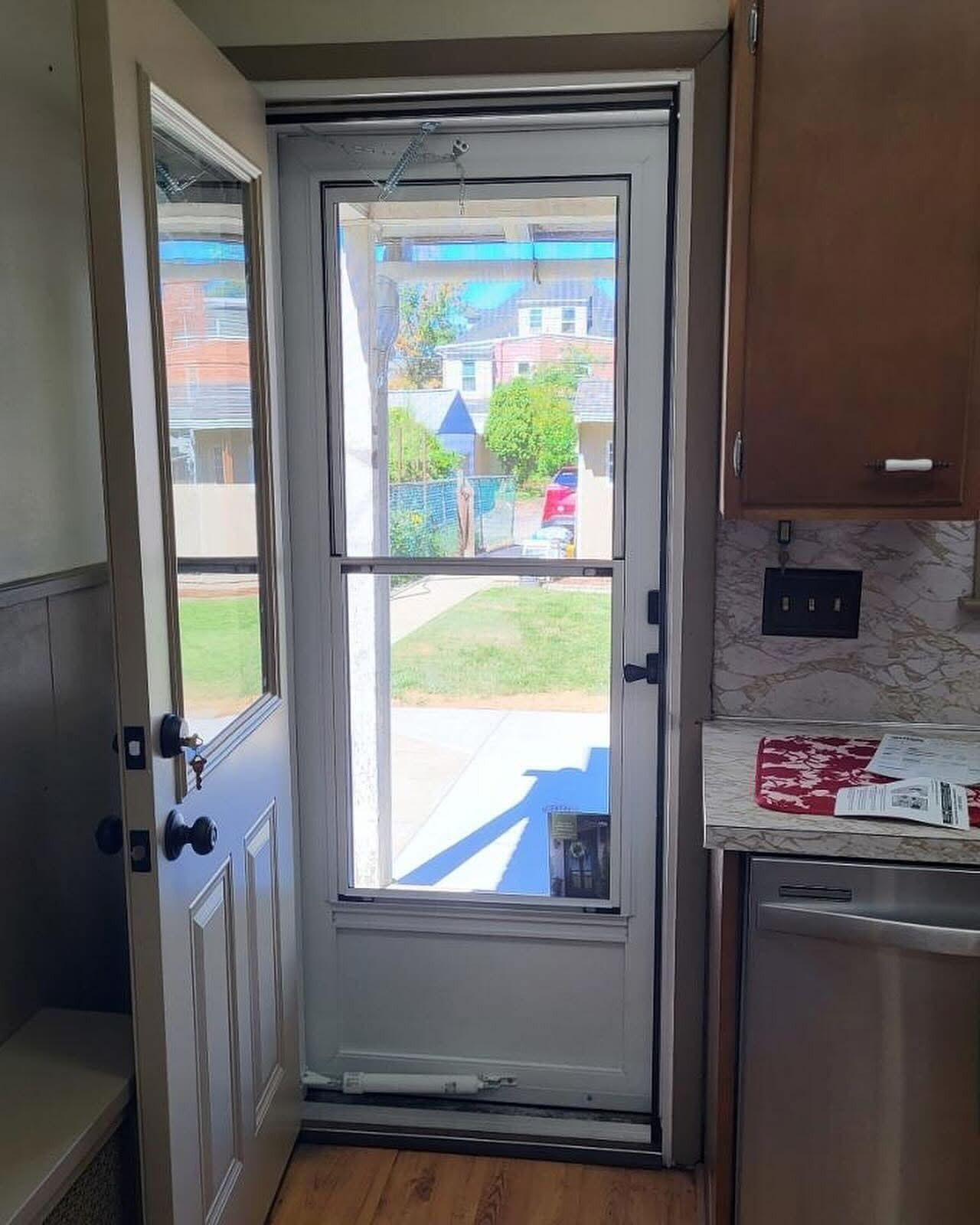 White screen door and open wooden door lead outside, viewed from a kitchen.