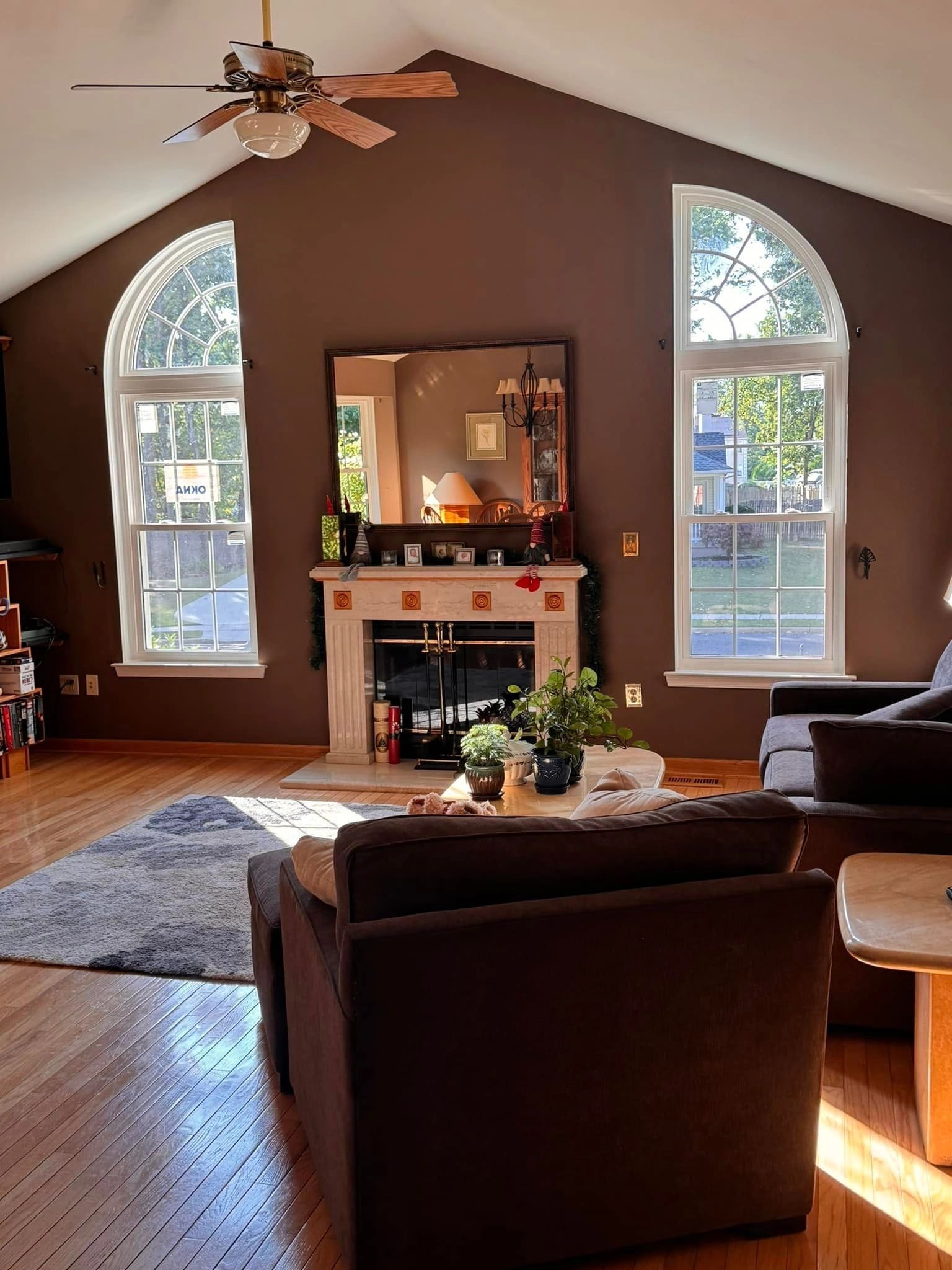 Living room with brown walls, fireplace, arched windows, and brown furniture.