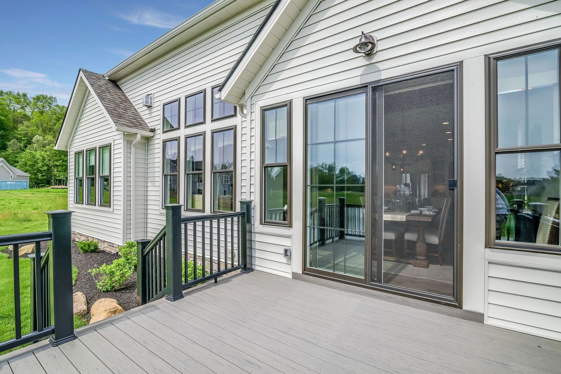 Exterior of a white house with a deck. Sliding glass door and multiple windows with black trim. Gray deck and black railings.