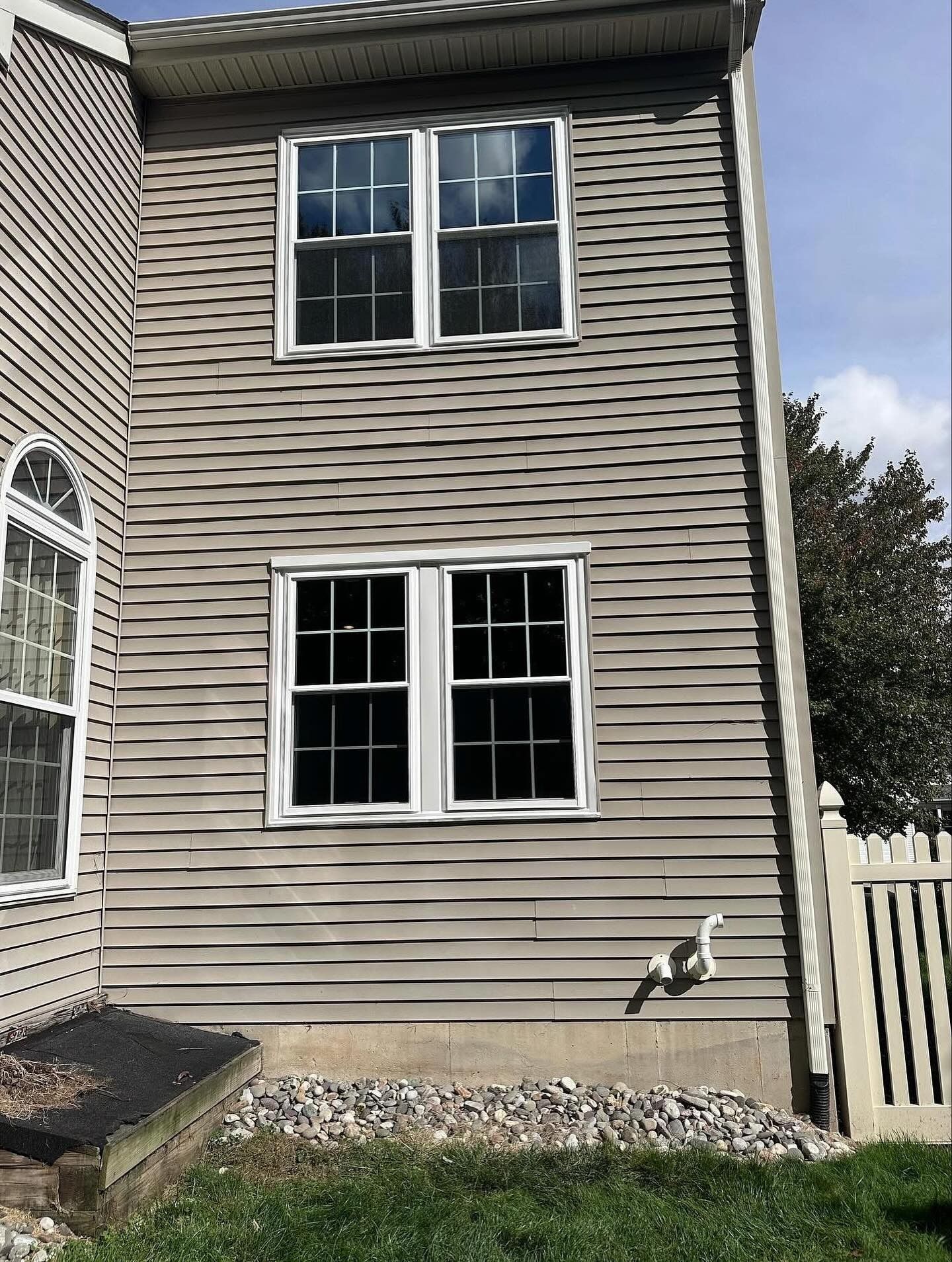 Exterior of a two-story building with two sets of windows and gray siding, near a white fence.