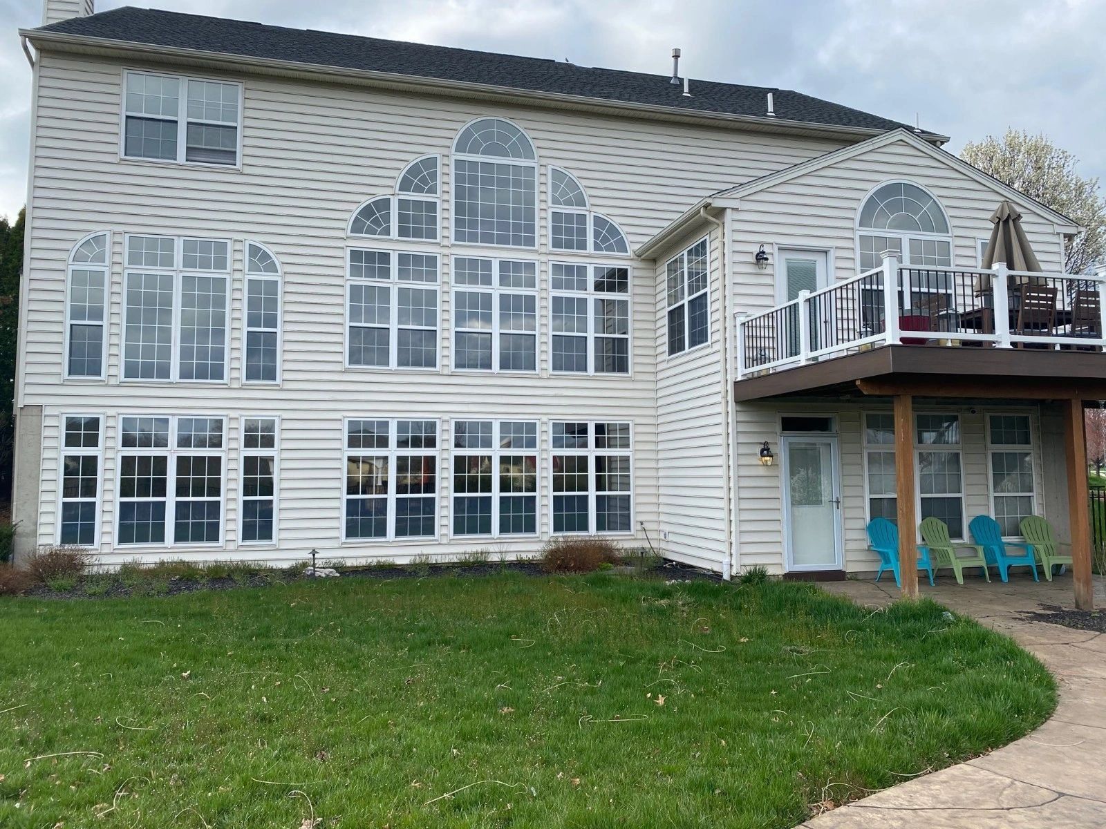 Back of a two-story beige house with large windows, a deck with seating, and a grassy yard.