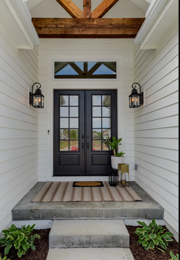 A white house with a black door and a rug on the porch