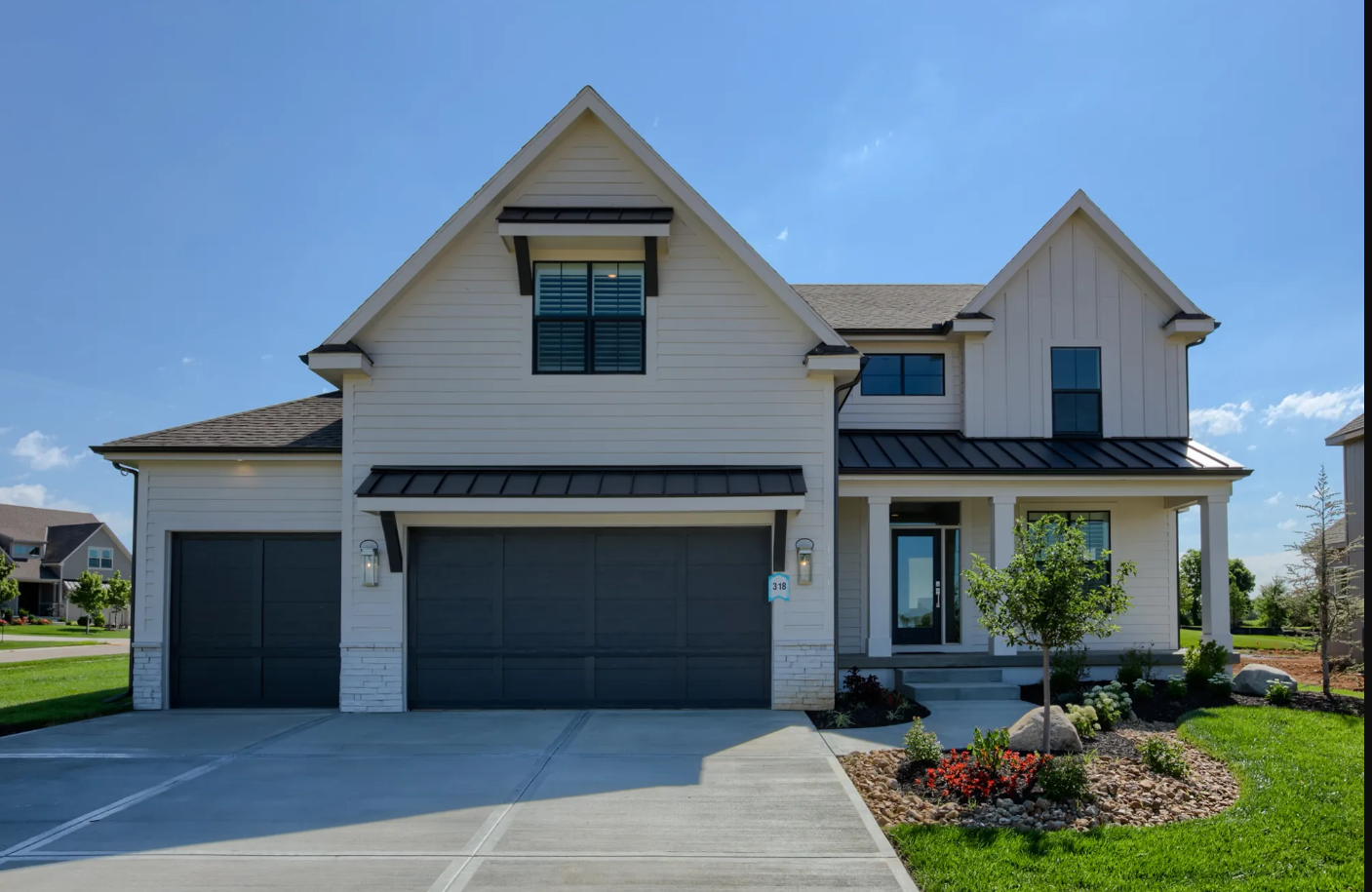 A large white house with a black garage door is sitting on top of a lush green field.