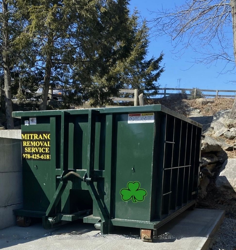 Green dumpster with a shamrock logo, sitting outdoors.