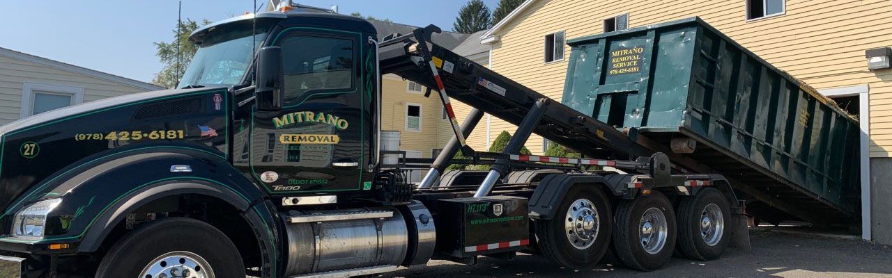 A dark green roll-off truck with a dumpster in a residential area. The dumpster is being tilted.