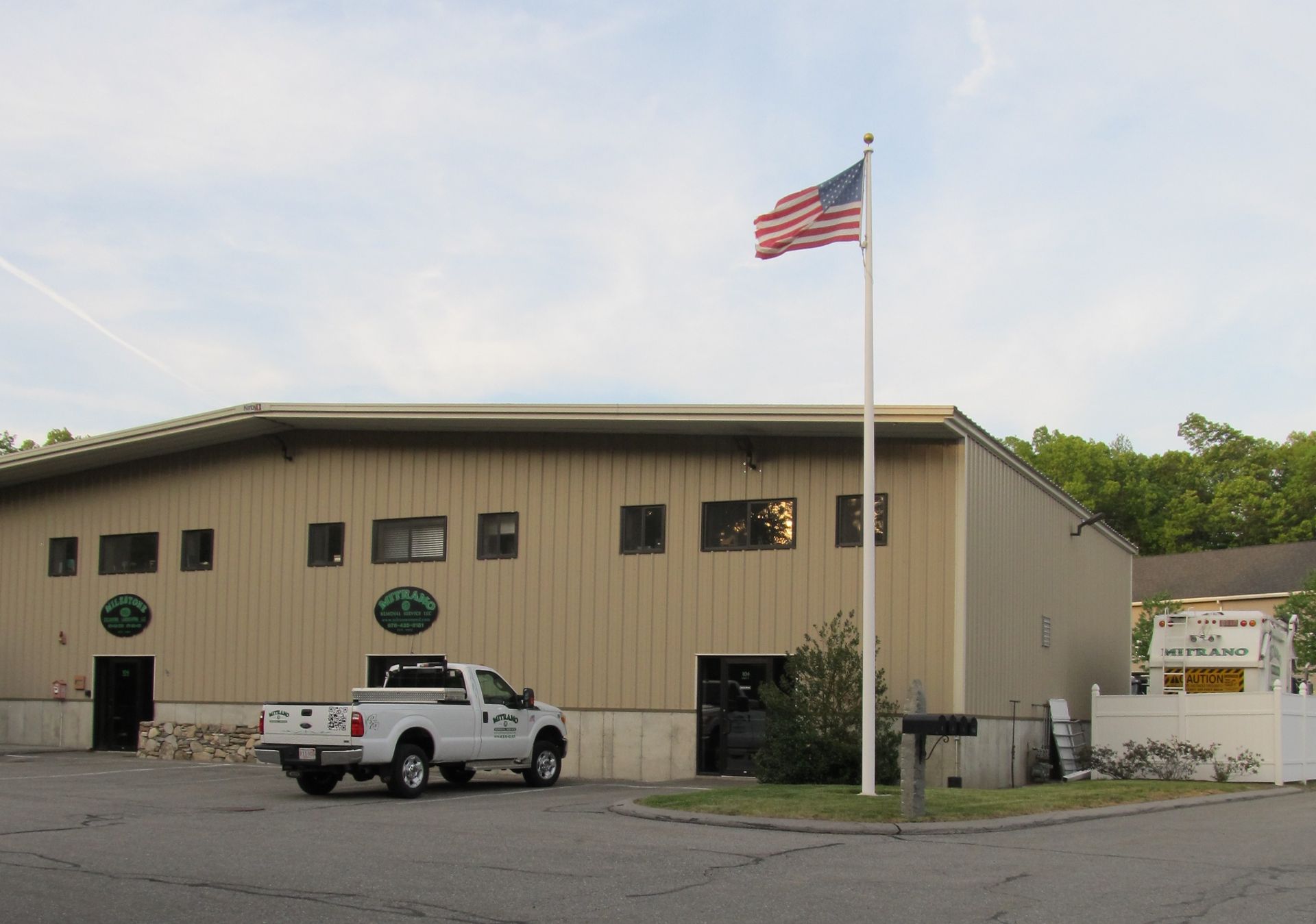 Beige commercial building with an American flag and a white pickup truck.