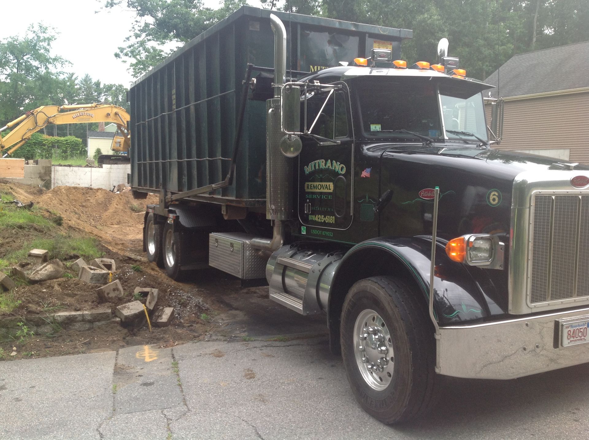 Dark green dump truck parked at a construction site with an excavator in the background.