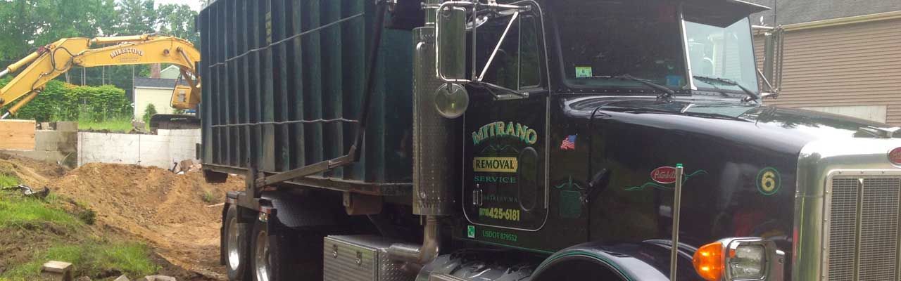 A black dump truck next to an excavator at a construction site. Green grass and dirt are visible.