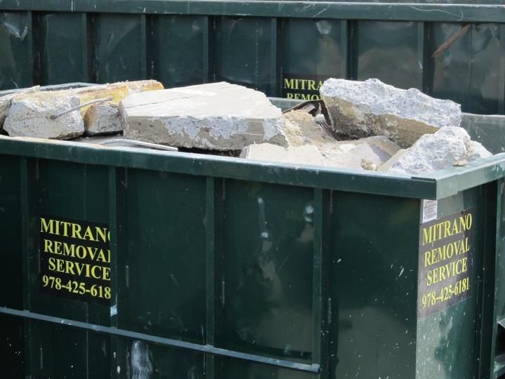 Dark green dumpster filled with concrete rubble; 