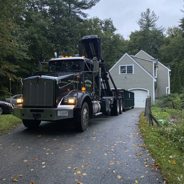 Black dump truck on driveway next to house, trees in background.