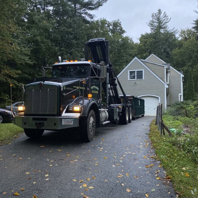 Black dump truck on driveway next to house, trees in background.