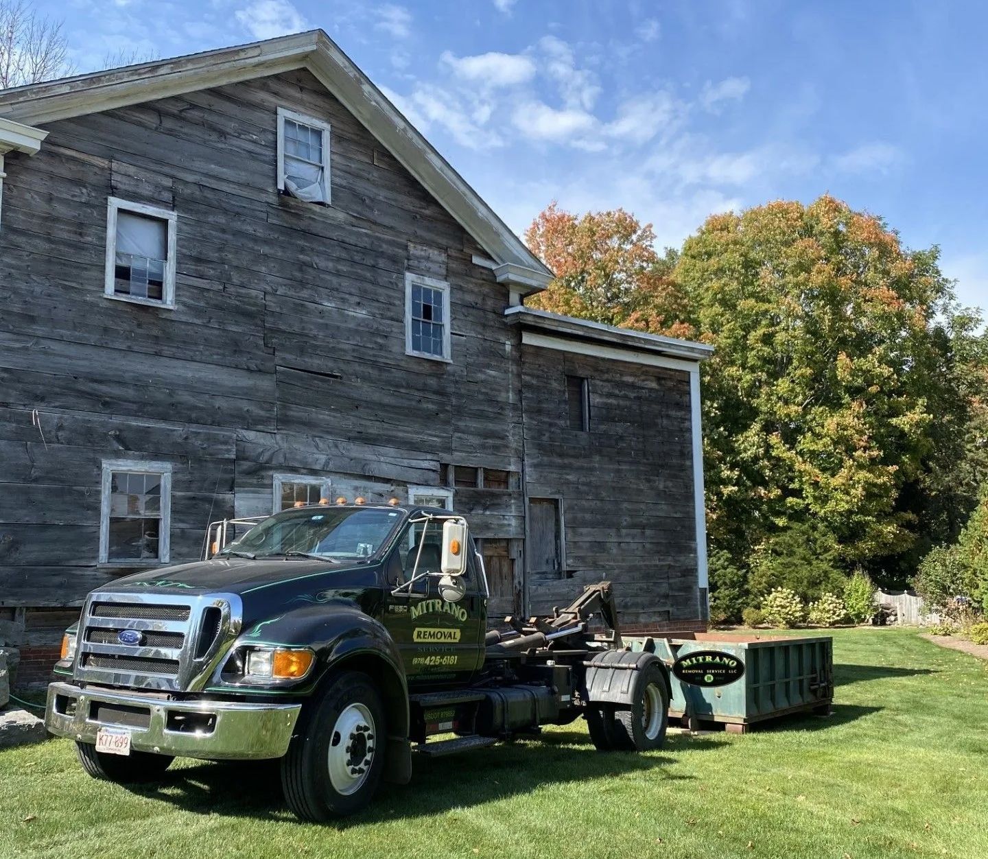 Black tow truck on a lawn beside a weathered gray house under a blue sky.