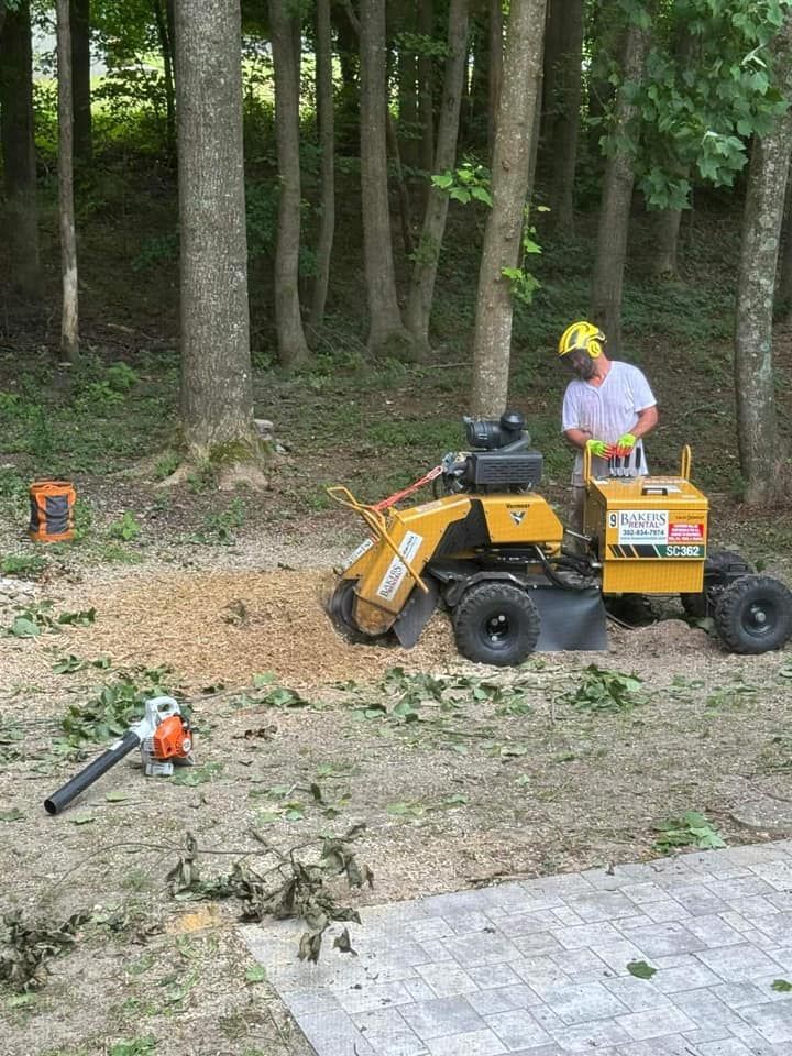 Man operating a yellow stump grinder in a wooded area, wearing a helmet and gloves.