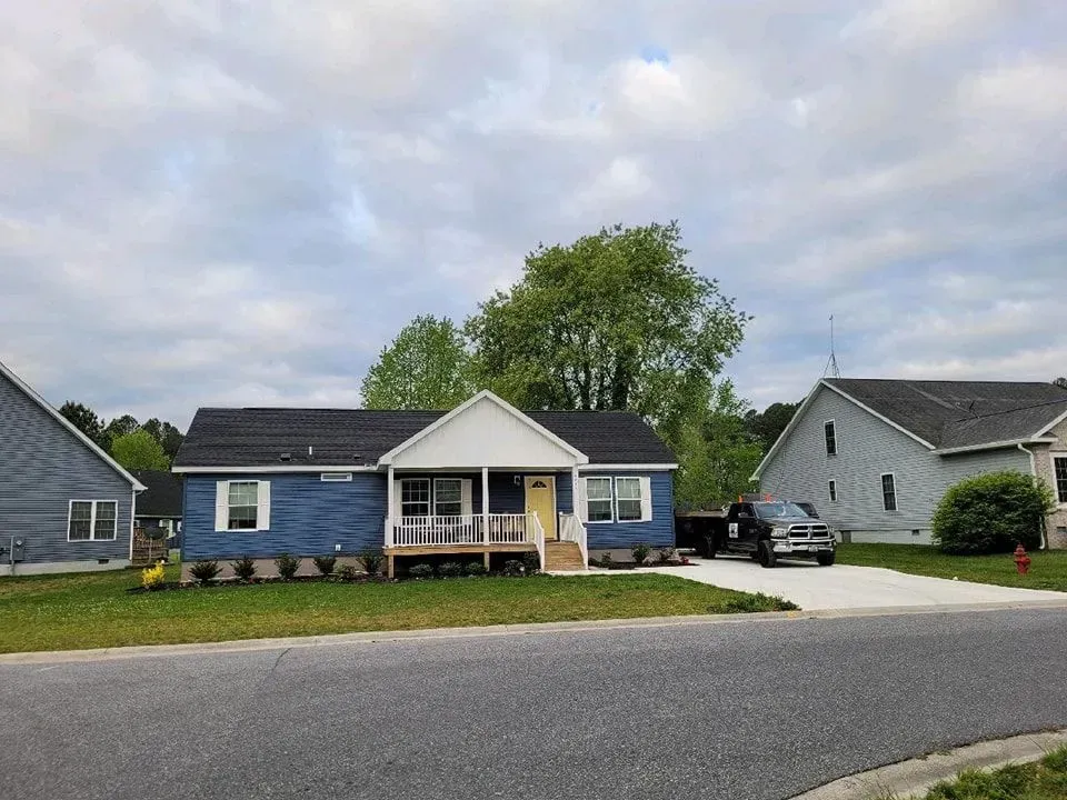 Blue house with white trim, yellow door, green lawn, cloudy sky, driveway with truck.