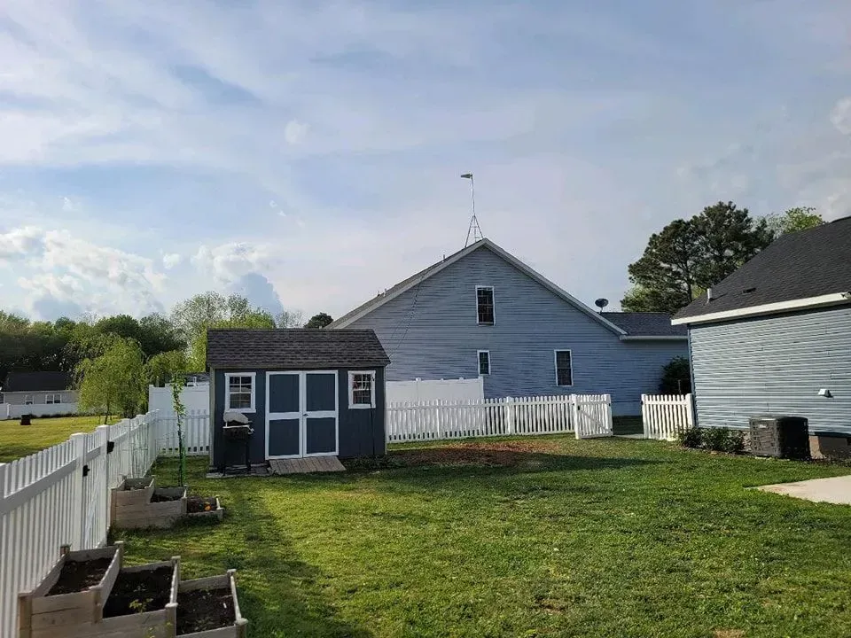 Blue backyard with a small shed, fence, and a large blue building in the background under a cloudy sky.