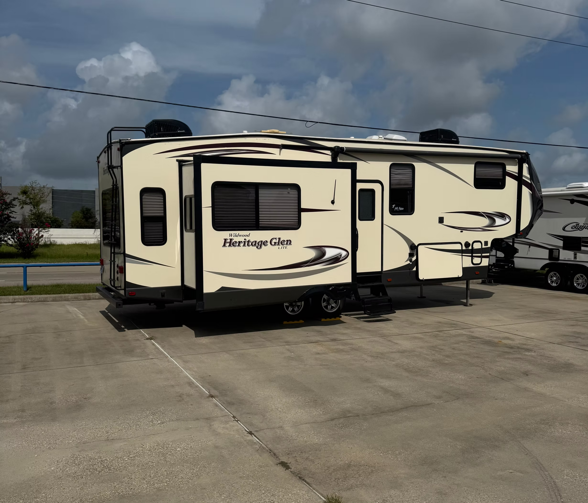 Cream-and-black Heritage Glen RV parked in a lot under cloudy skies.
