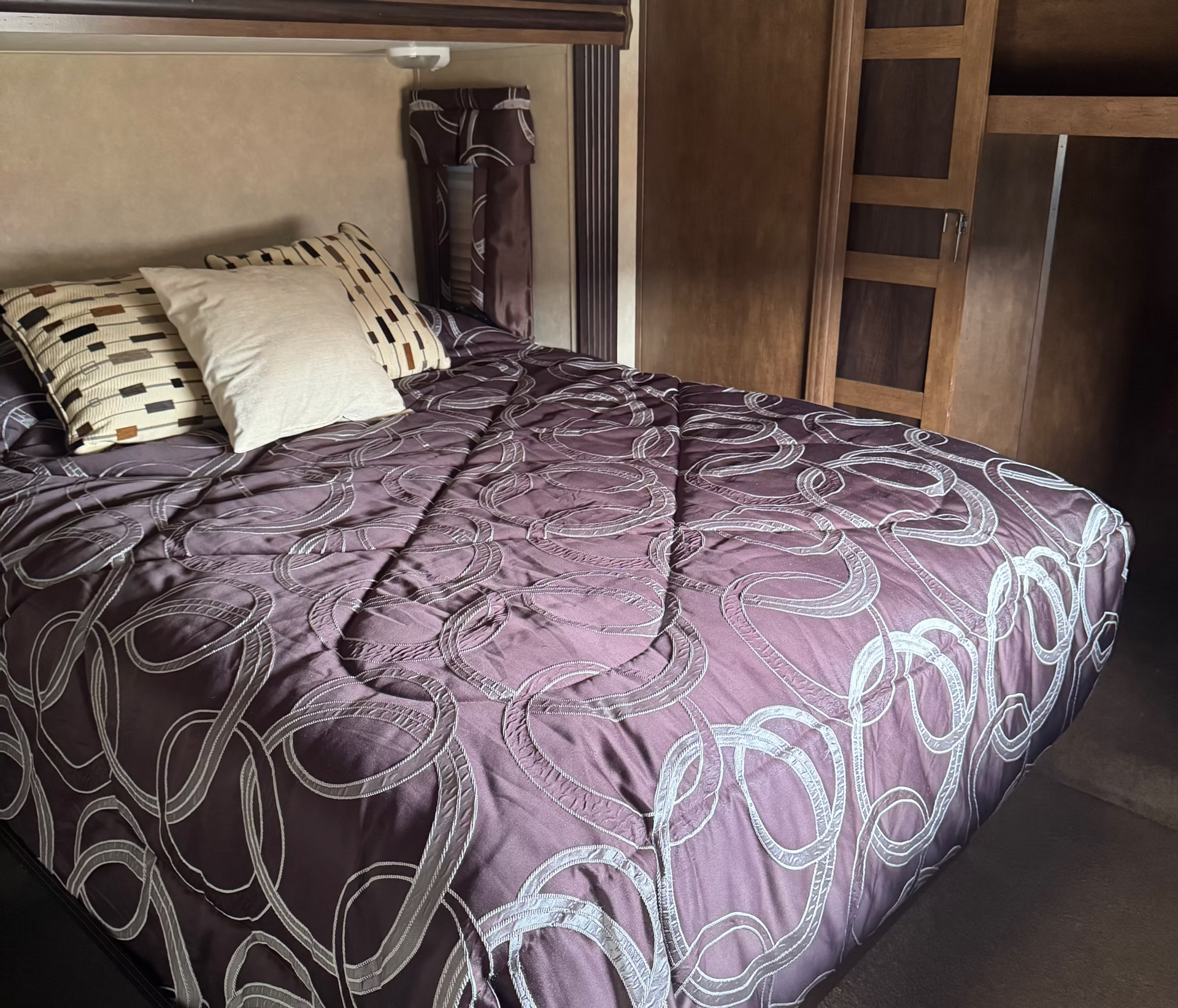 Neatly made bed with a purple patterned comforter and two pillows in a wooden bedroom alcove