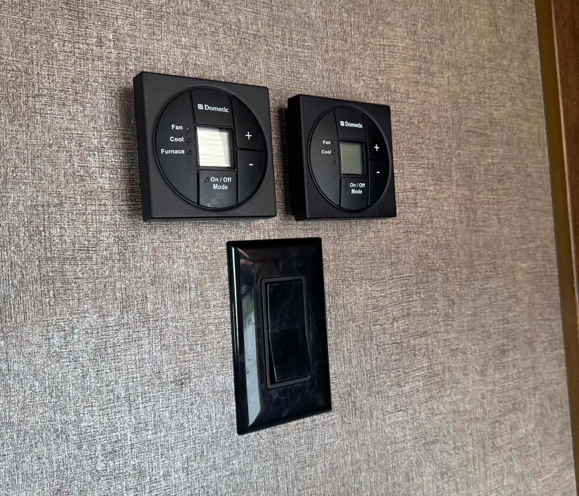Two black wall-mounted controls above a rectangular wall opening on a textured beige wall