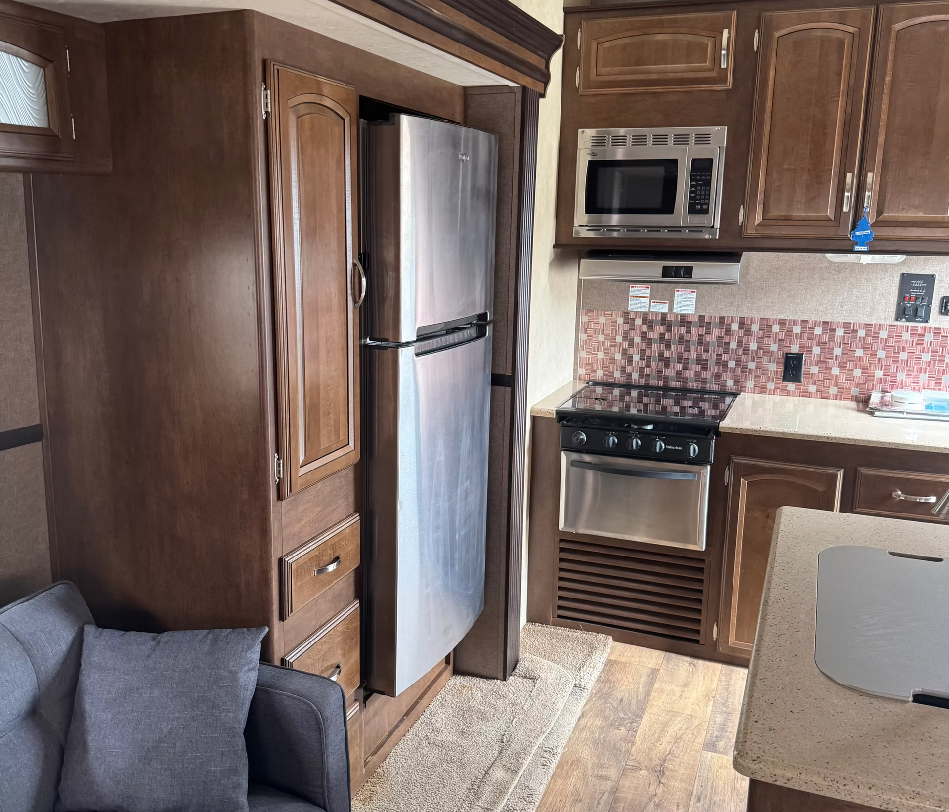 Compact kitchen with dark wood cabinets, stainless fridge, microwave, stove, and tiled backsplash.