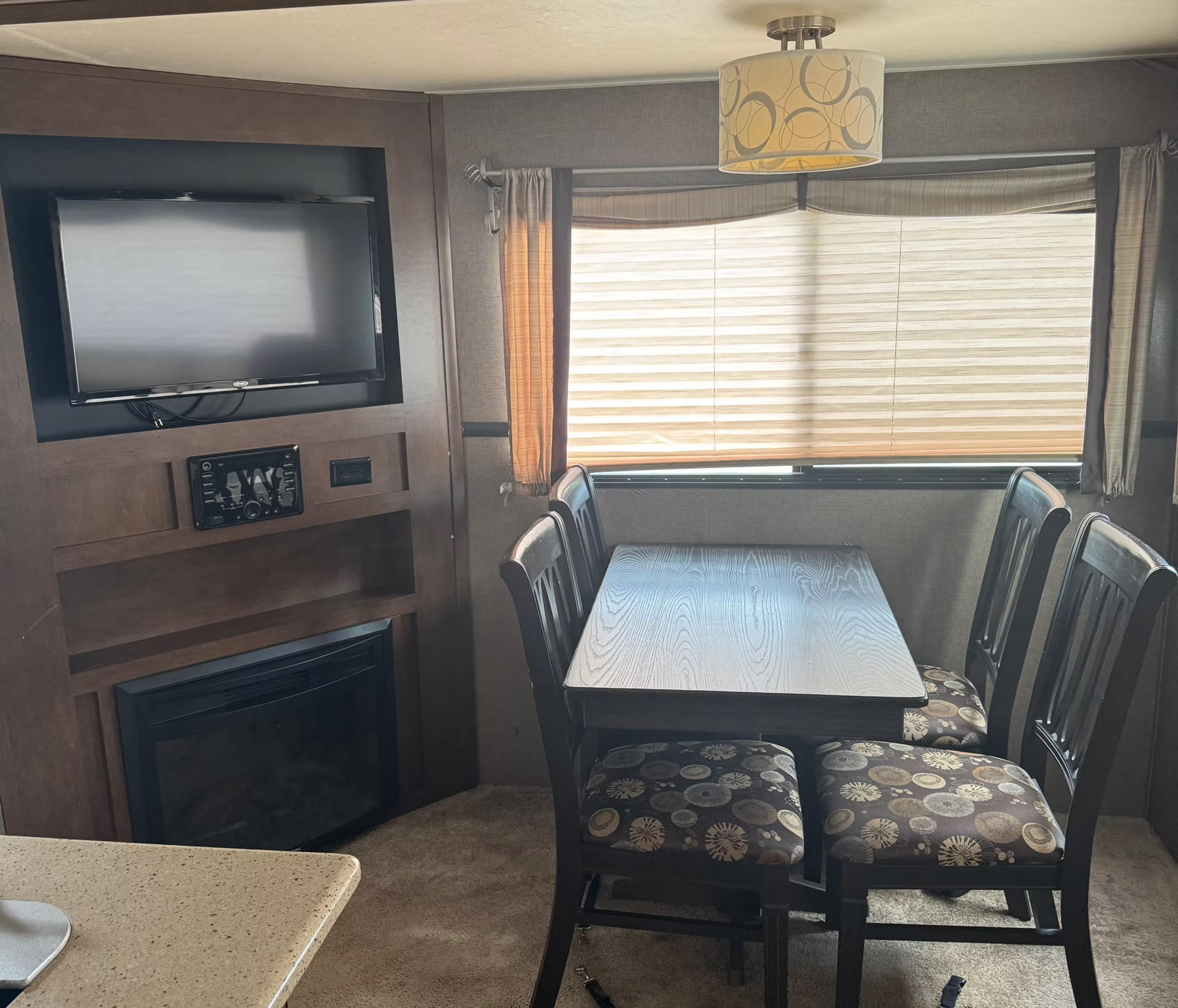 Cozy RV dining area with table, bench seating, wall-mounted TV, and fireplace by a window