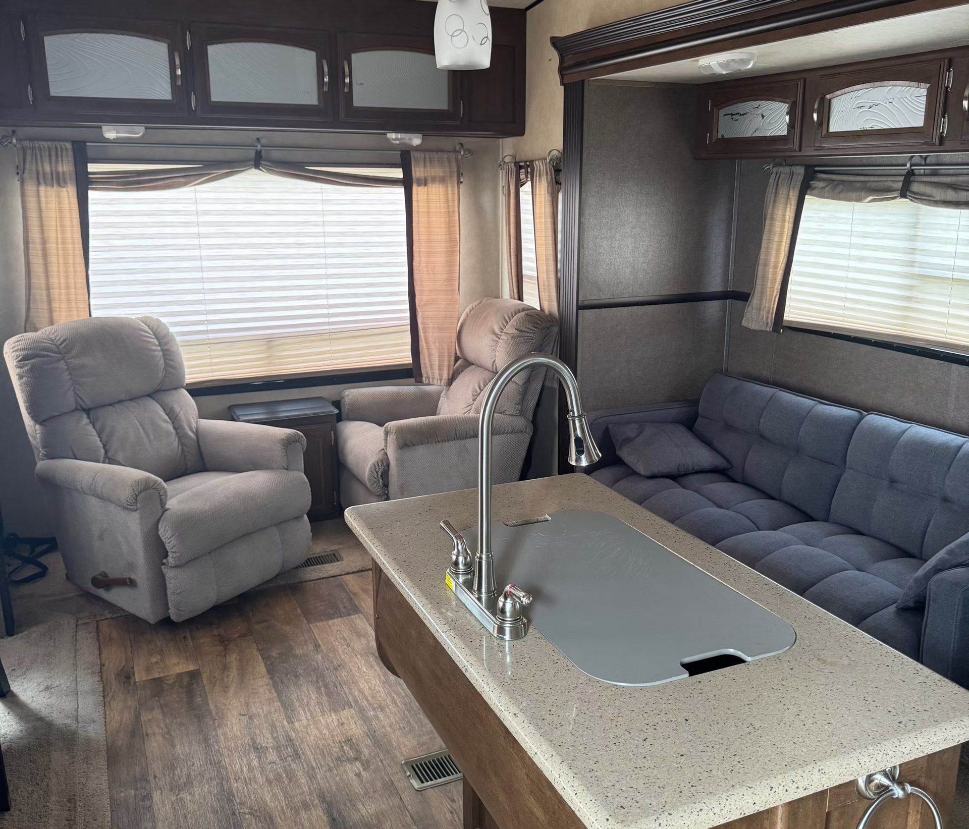 Cozy RV living room with gray recliners, a sofa, and a kitchen island with sink