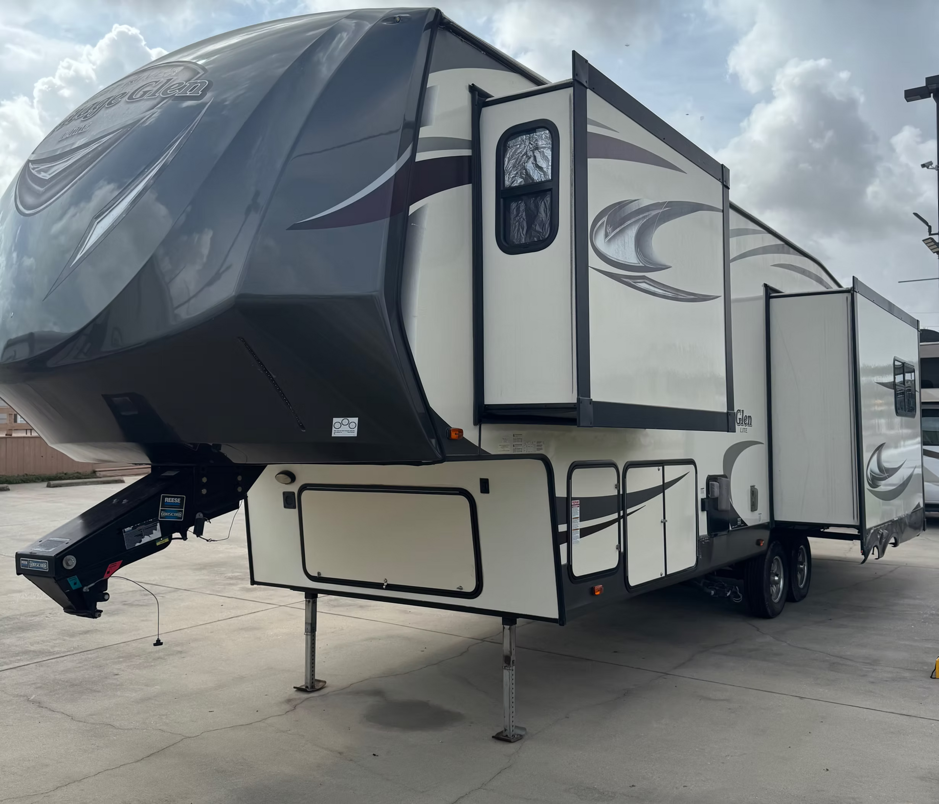 White and black fifth-wheel RV trailer parked on a lot under cloudy skies