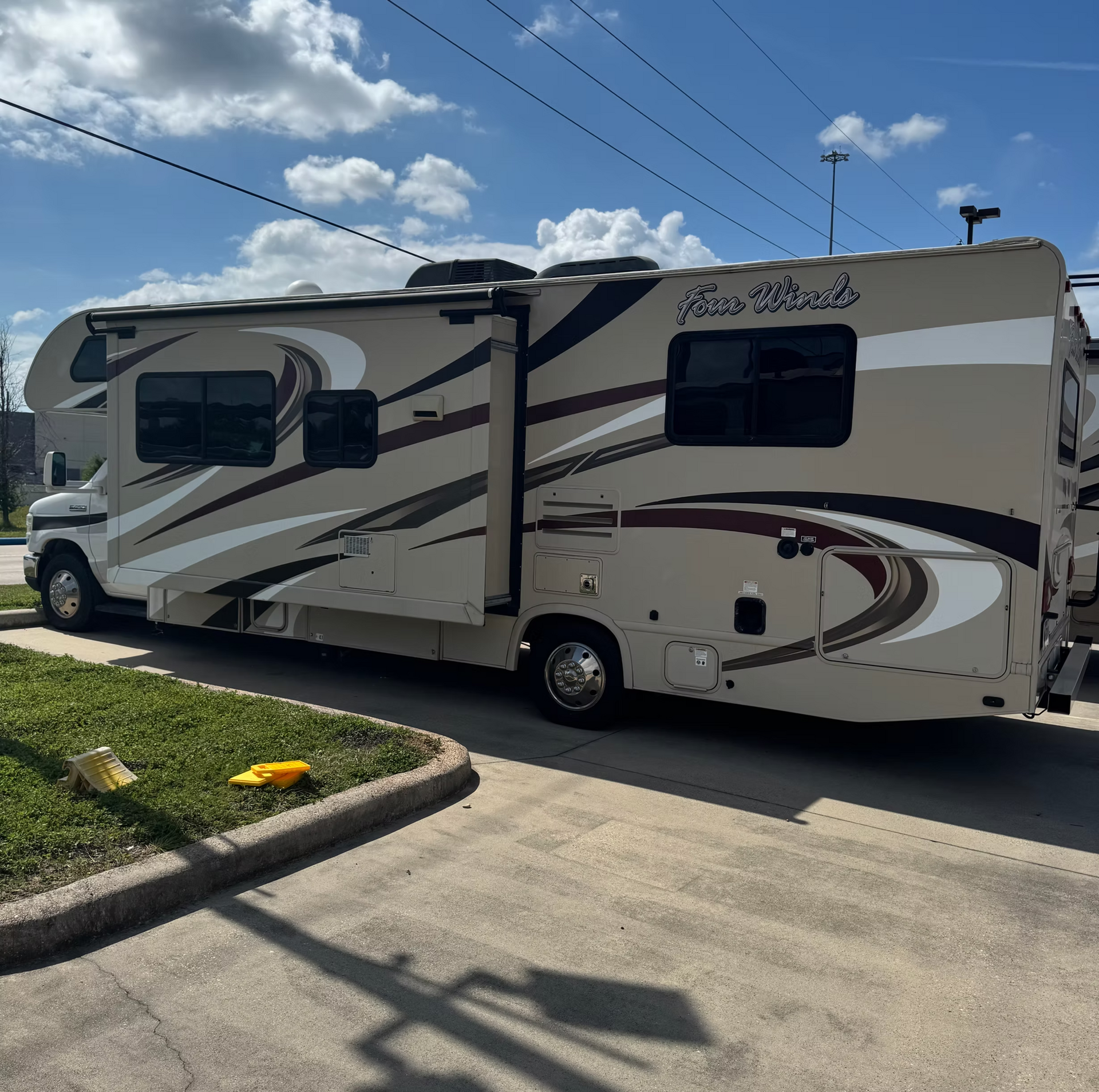 Large beige and gray RV parked on a suburban street under a blue sky with clouds