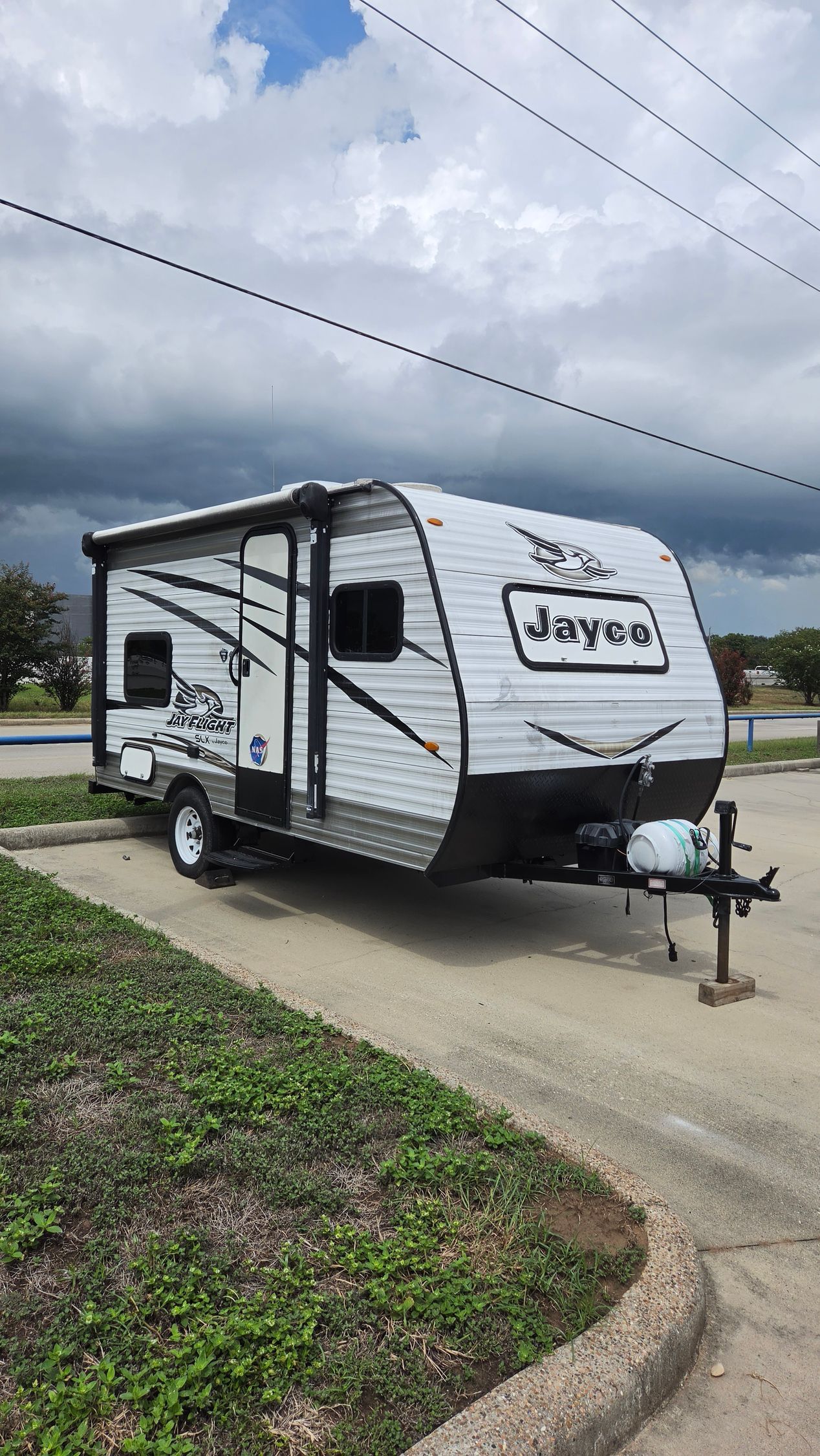 White and black Travel Lite camper trailer parked on a driveway under a cloudy sky.