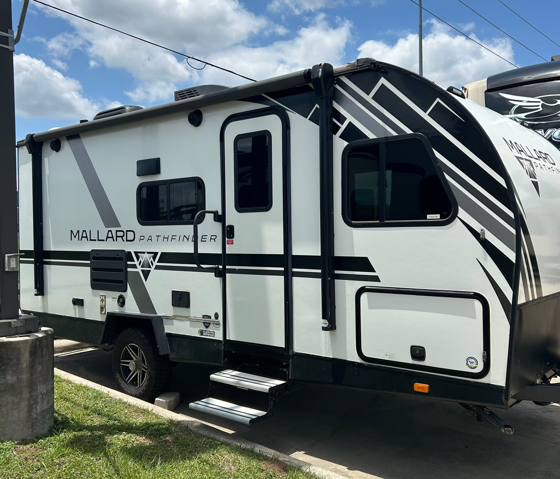 White and black travel trailer parked on grass under a blue sky