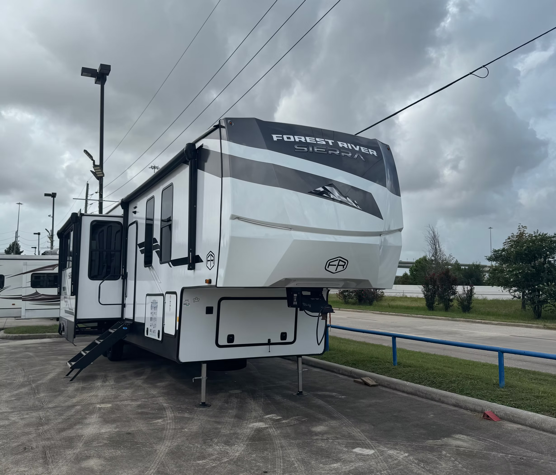 White travel trailer parked on a wet roadside under cloudy skies, with an awning and steps extended.