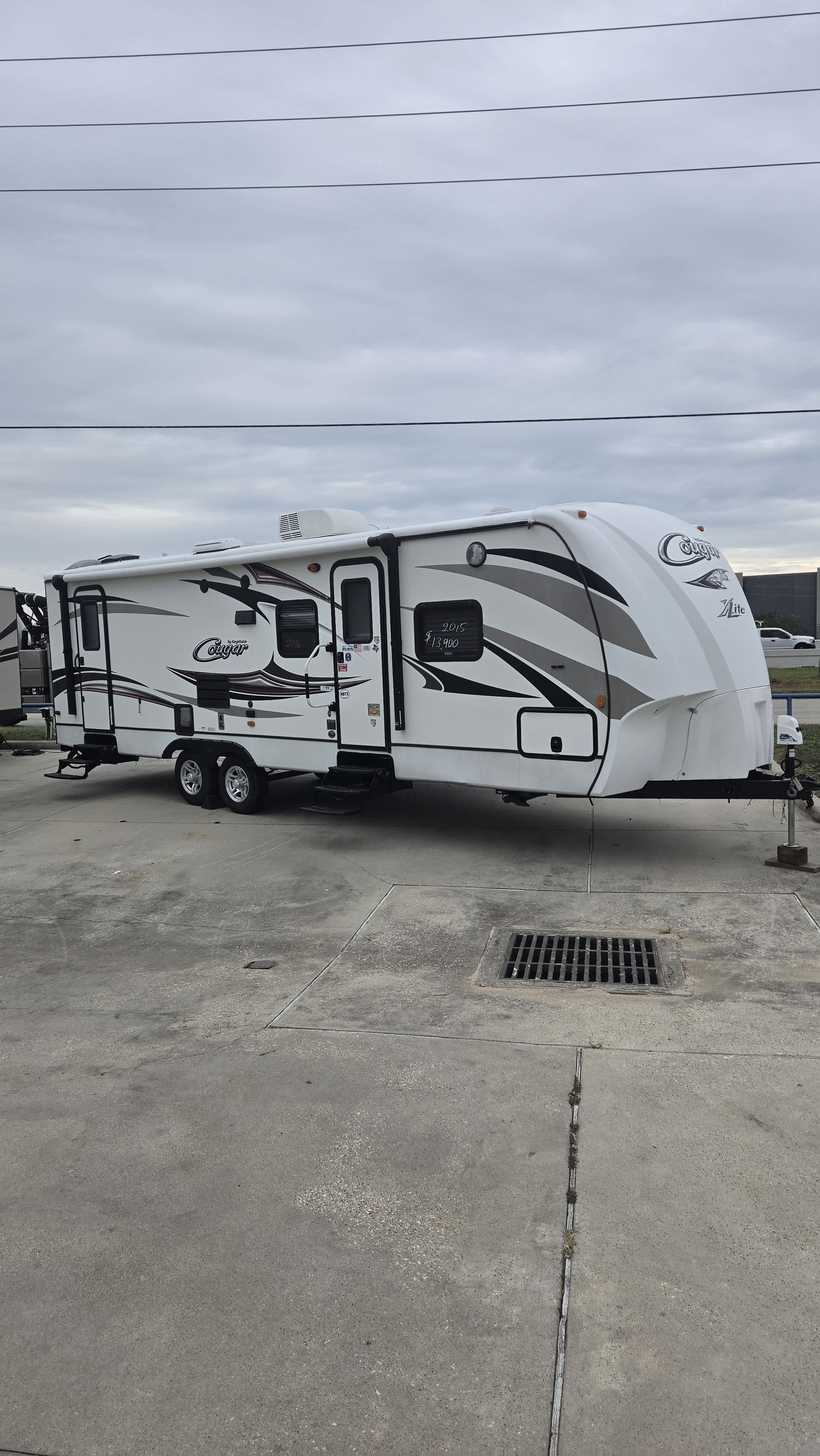 White travel trailer parked on a concrete lot under a cloudy sky, with utility hookups visible.