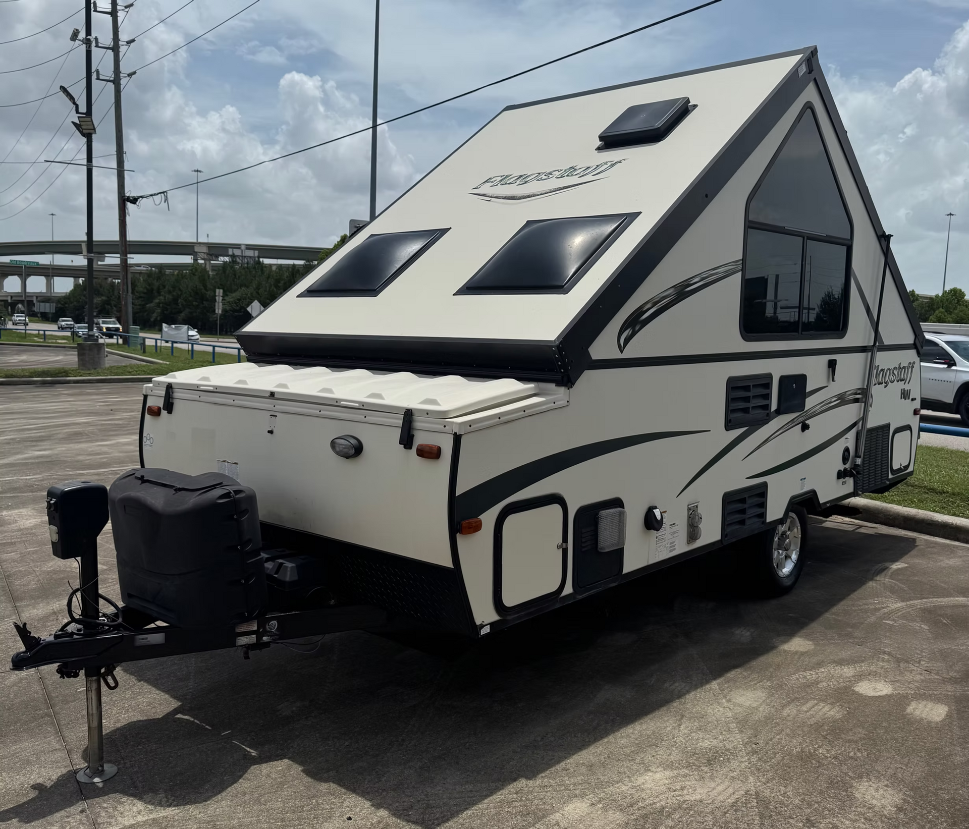 White pop-up camper trailer parked in a lot, with a front hitch and roof windows.