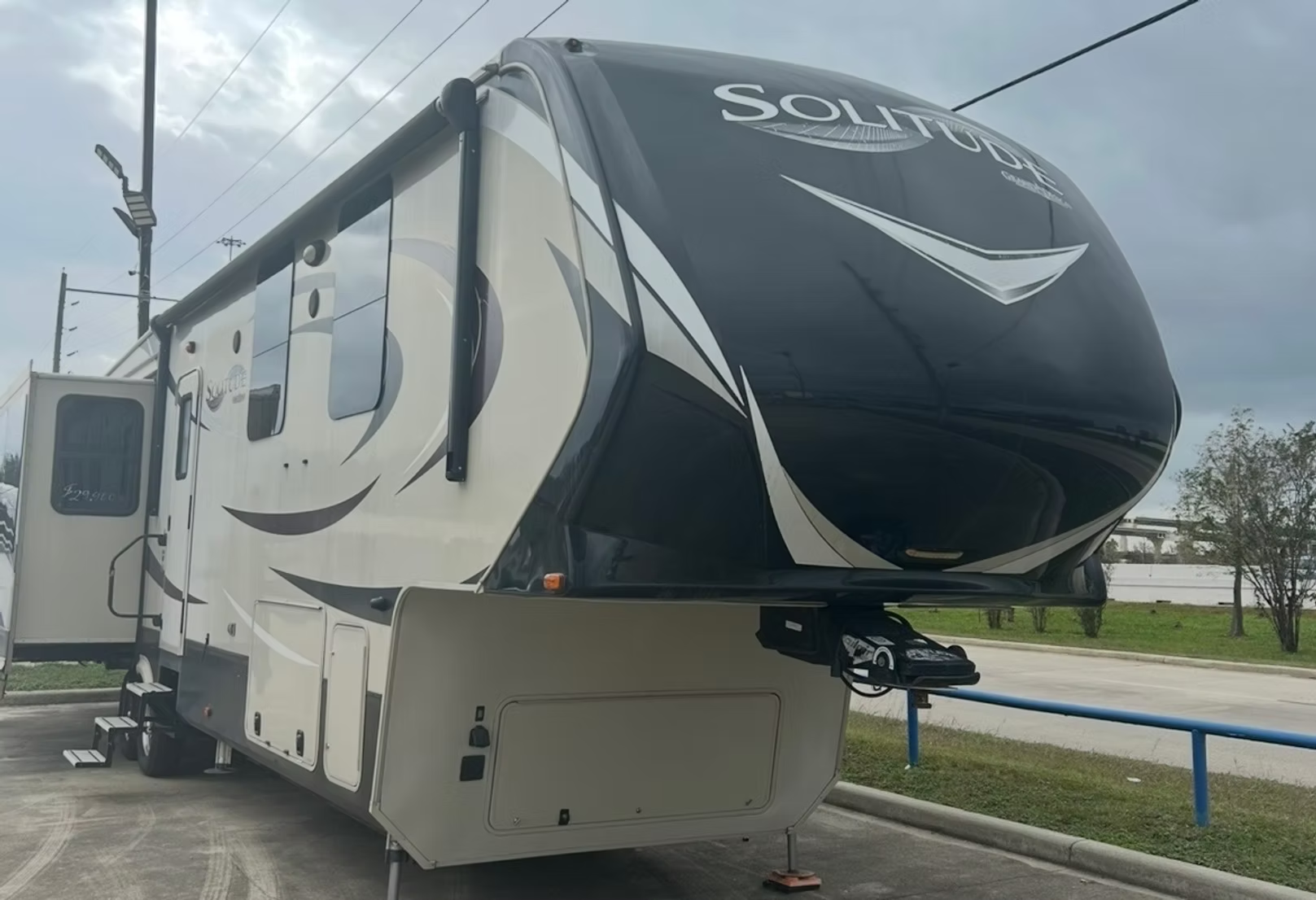 Black-and-white Solitude fifth-wheel RV parked in a lot under cloudy skies.