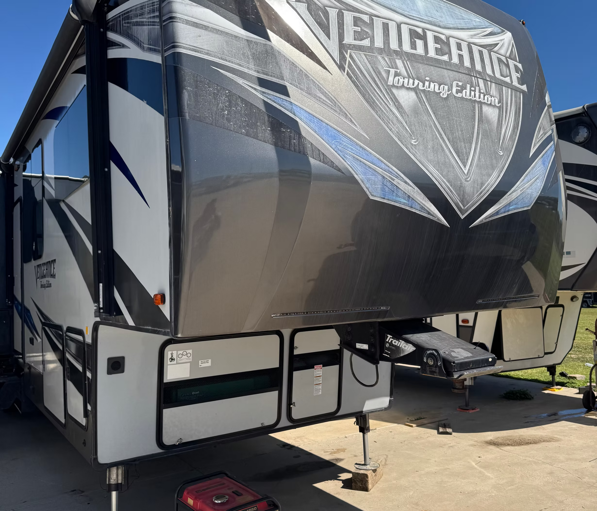 Black and gray Vengeance fifth-wheel trailer parked outdoors in a driveway, front view.